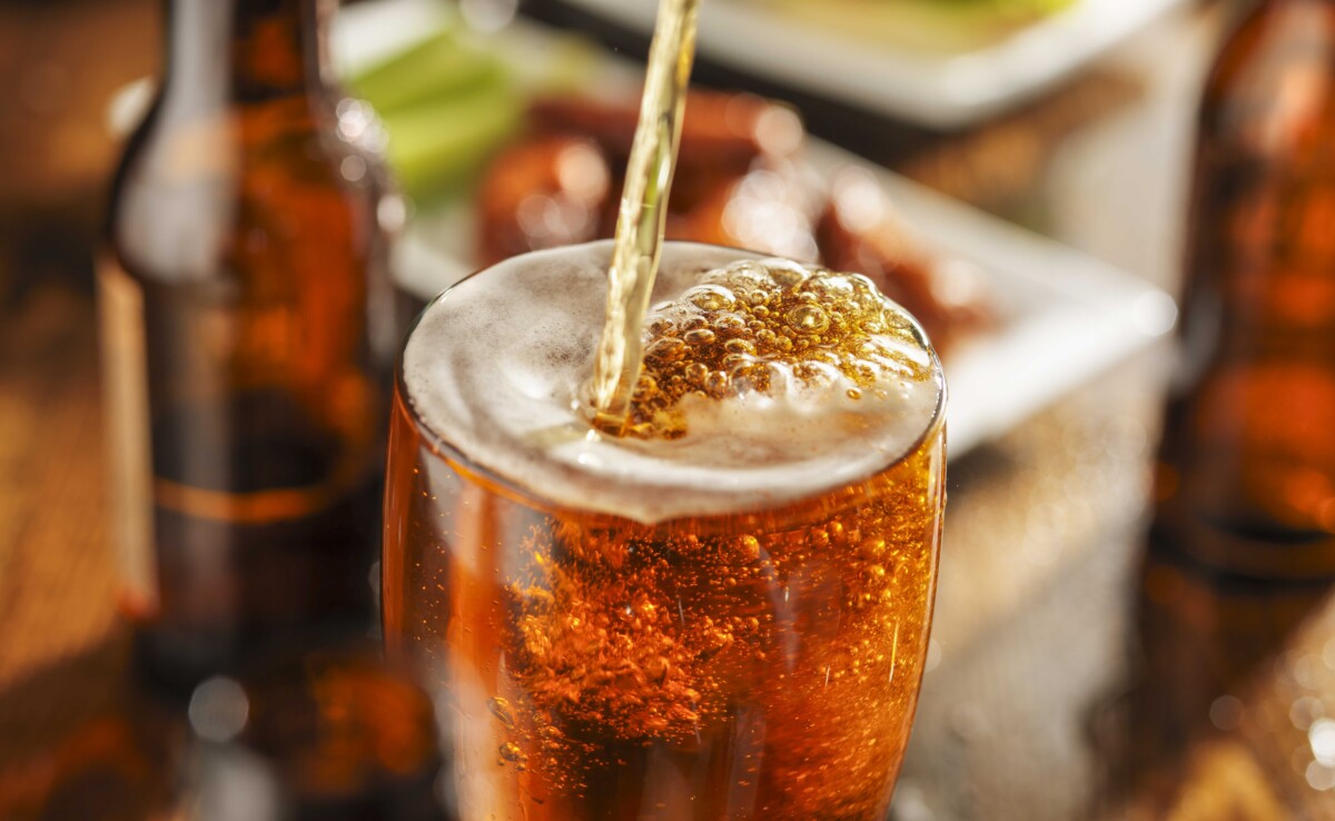 pouring beer into glass with bbq chicken wings in background